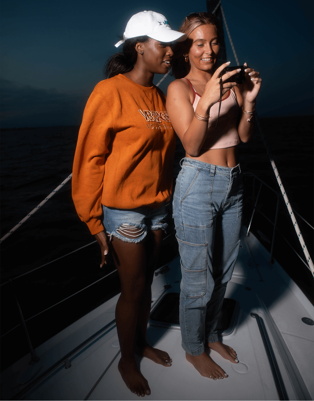 Two women on a boat at night, taking a photo with a phone.